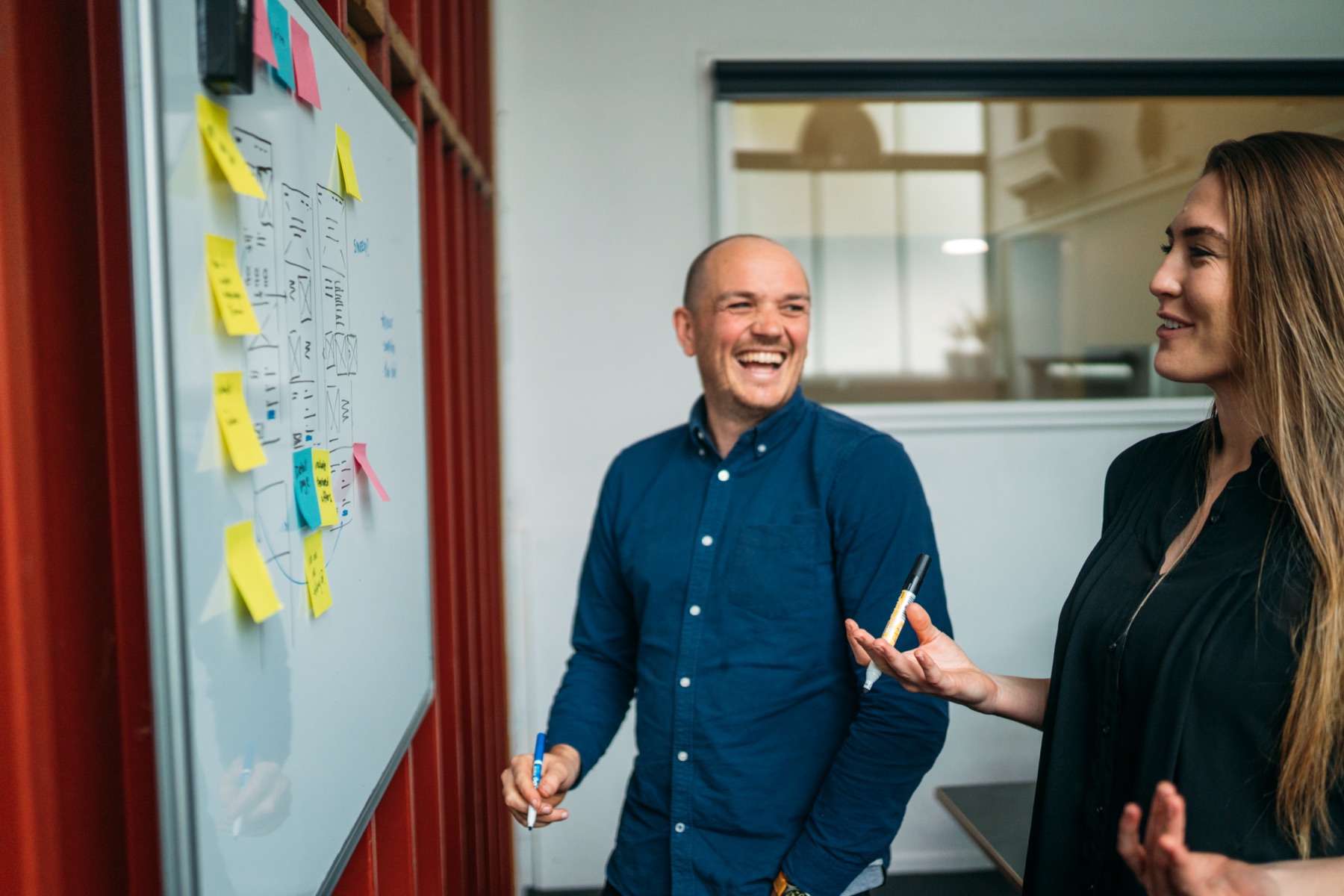 Two people working on a whiteboard, laughing